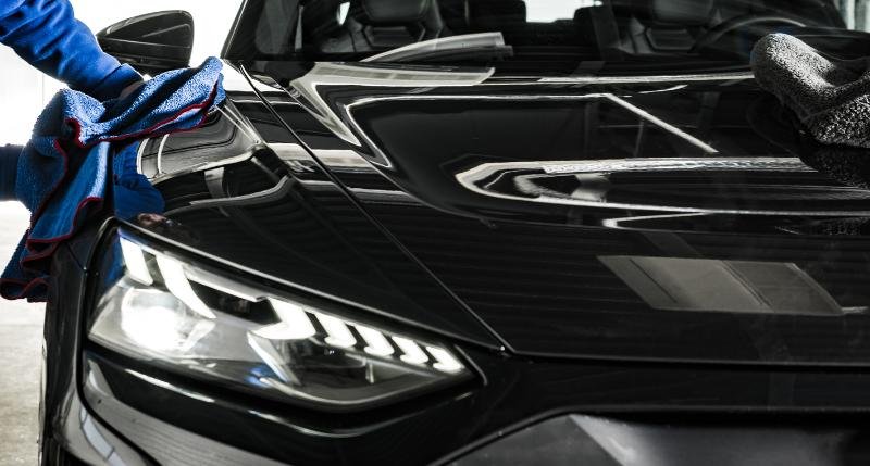 Hand detailing the bonnet and headlight of a black luxury sports car in Perth